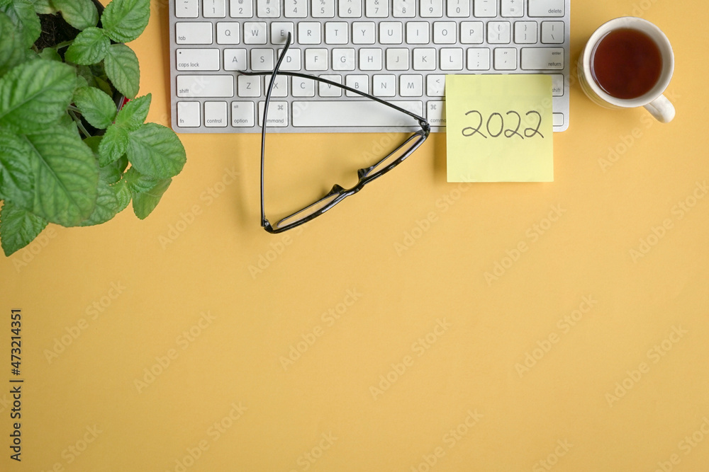2022 written on yellow paper stick on top of keyboard with coffee, eyeglasses and plant. Flat lay, copy space. 2022 written on yellow paper stick on top of keyboard with coffee, eyeglasses and plant. Flat lay, copy space.