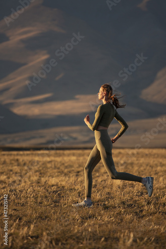 A sportive girl goes jogging against the backdrop of the sunset mountains.