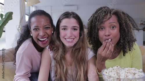 Three excited young women playing video games on a console in the living room - Multiracial female friends having fun together on social online entertainment platform - Technology and leisure concept photo
