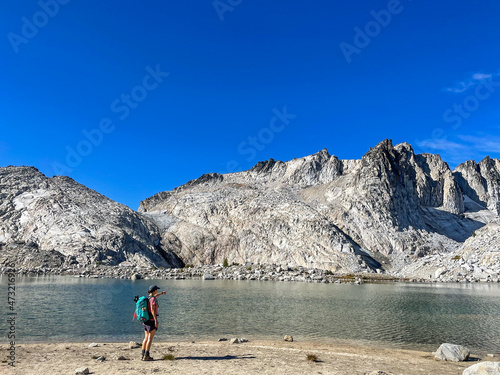 female hiker standing in front of blue alpine lake and pointing at rugged mountain