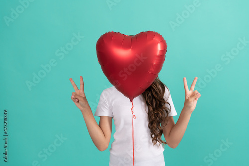 teen girl hiding behind red heart party balloon for valentines day love symbol peace geature, peace photo