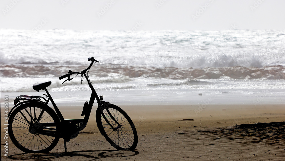 Fototapeta premium Abandoned bicycle on the sand, strong sea bottom and big waves.