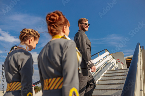 Aviation captain and stewardesses walking up airplane stairs