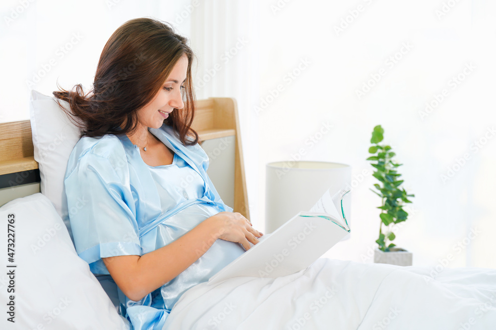 happy pregnant woman sitting on bed reading book at home happy pregnant woman sitting on bed reading book at home