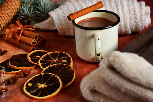 Winter warming drink hot chocolate and cinnamon sticks in tin bowl  woman gloves and white scarf on table decorated with spices  star anise  slice of dry lemon and branch of christmas tree and cones