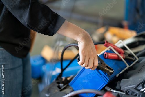 Asian young woman holding a tablet on her hand and inspecting an old vehicle battery, woman recharge a car battery from other battery. Asian woman fixing her car herself.