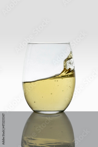 crystal glass with moving white wine making waves and white background