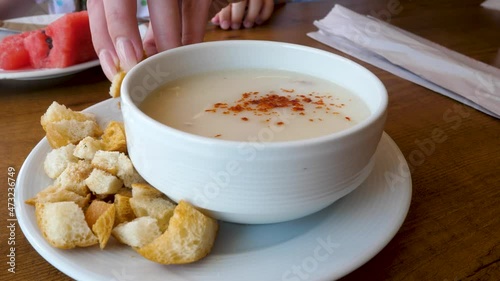 Woman's hand put bread cubed or croutons in cream soup. Add flavor to dish and eaten as snack food. Piece of rebaked bread cubed and seasoned. Paprika spice made from dried and ground red peppers photo