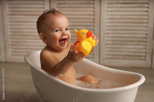 Fotografering a baby of 11 months is bathing in a white baby bath with rubber ducklings, the baby is laughing, the concept of children's goods
