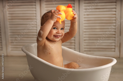 Fotografia a baby of 11 months is bathing in a white baby bath with rubber ducklings, the baby is laughing, the concept of children's goods