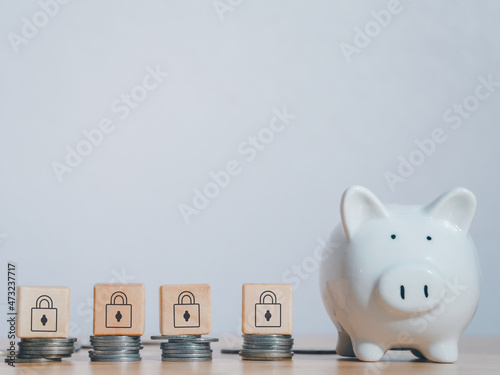 White piggy bank near stack coins with wooden padlock block on top on table to security of money invest for future. Concept for loan, property ladder, financial,real estate investment,taxes and bonus.