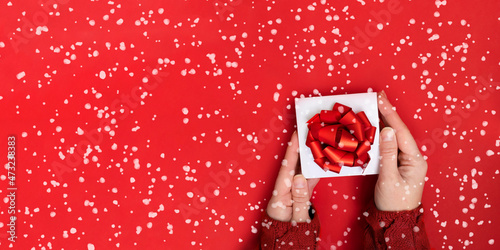 hands holding white gift box with red ribbon bow on red background. present for Christmas, new year, valentine day