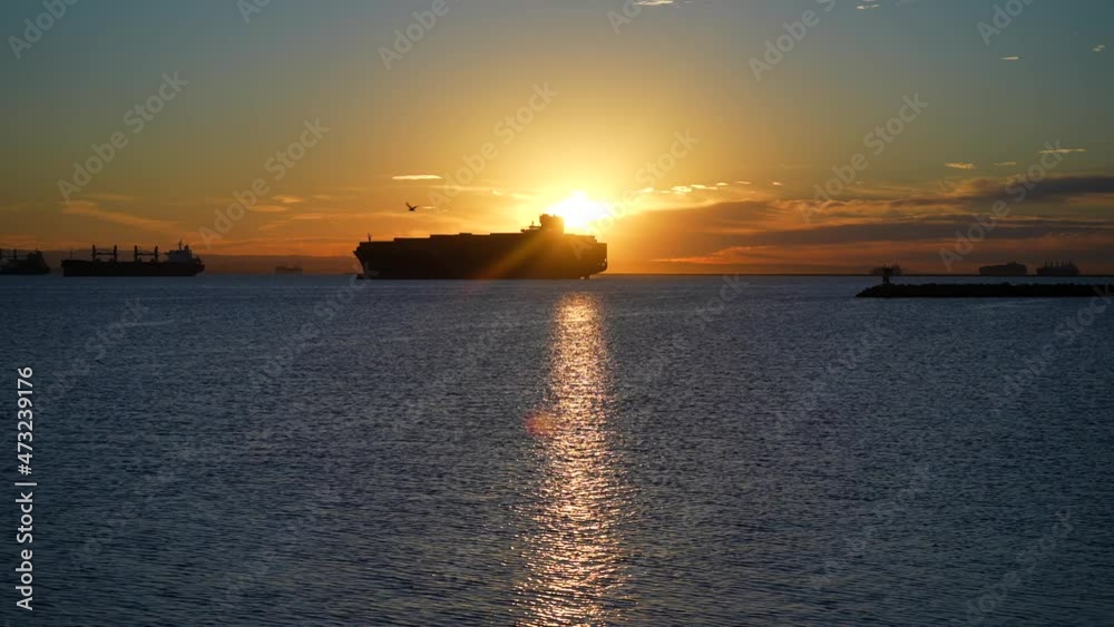 Silhouette of a cargo container ship in the harbor amidst a global supply chain crisis at sunset Silhouette of a cargo container ship in the harbor amidst a global supply chain crisis at sunset