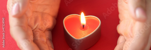 Women hands protect burning fire in candle in form of heart closeup