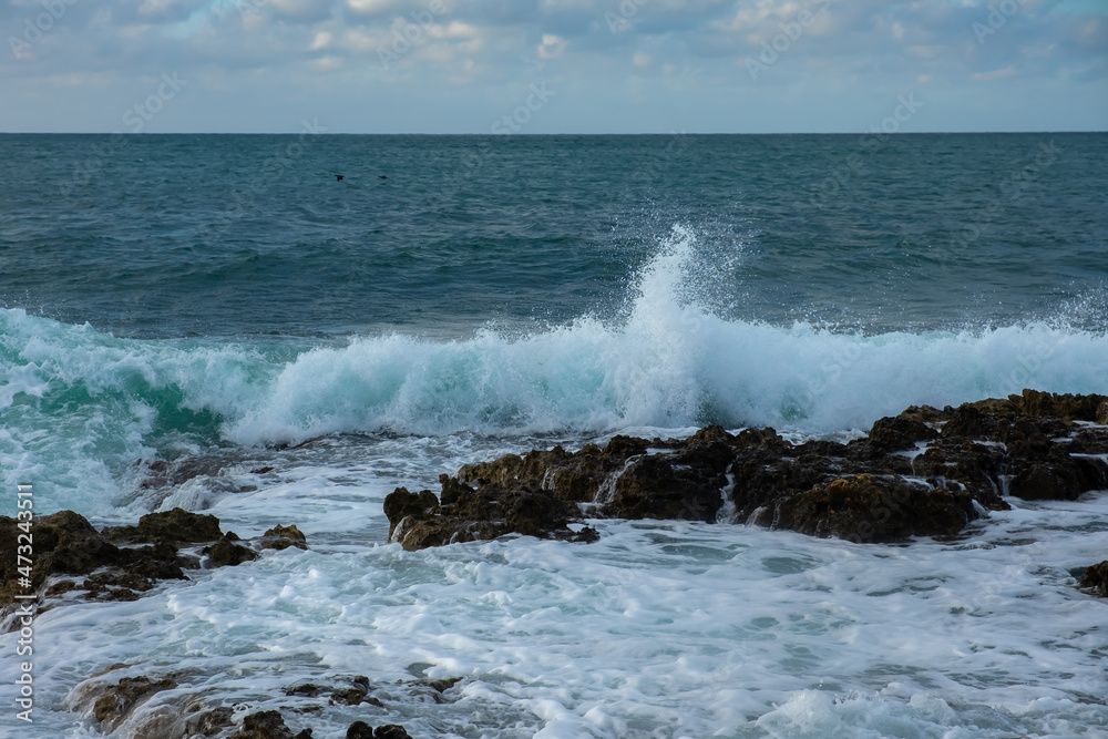 Turquoise sea stone beach, breaking waves on a cloudy spring day. Beautiful sea background. The concept of summer, vacation, travel. The purest clear sea water, large stones on the beach close-up