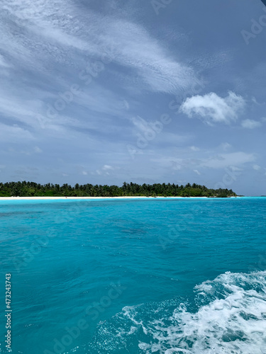 View of a white sand beach on the Maldives island from a boat in the turquoise water of the Indian Ocean © Elena