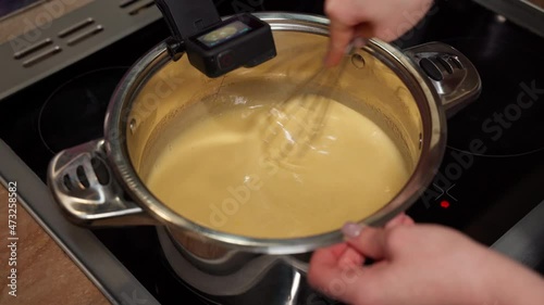 A professional blogger confectionery manufacturer kneads Christmas cake dough with a whisk. Step-by-step recipe for cooking cake in a pan on an induction cooker. Recording on an action camera photo