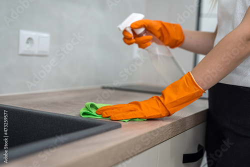 beautiful female hands in orange mittens wipe the kitchen surface from dust