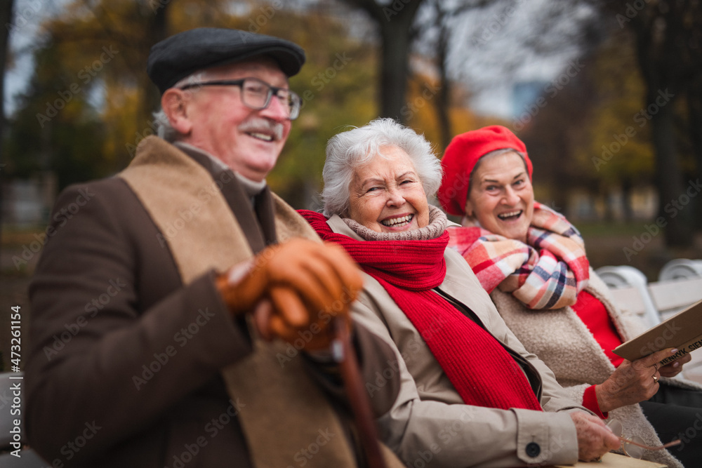 Group of happy senior friends sitting on bench in town park in autumn, looking at camera. Group of happy senior friends sitting on bench in town park in autumn, looking at camera.
