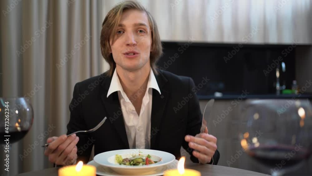 A young Caucasian man sits at a table during a candlelit dinner, eats a lot and talks non-stop, waves and gestures with his hands. A young Caucasian man sits at a table during a candlelit dinner, eats a lot and talks non-stop, waves and gestures with his hands.