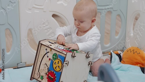 Cute baby boy playing with wooden busy board on montessori busy house. Educational toys. 8 month old baby boy wearing safety helmet enjoy playing time in baby playpen. High quality 4k footage photo