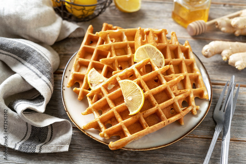 Ginger lemon waffles with honey in a ceramic plate on a light gray wooden culinary background. Delicious healthy homemade cakes that increase immunity on the kitchen table