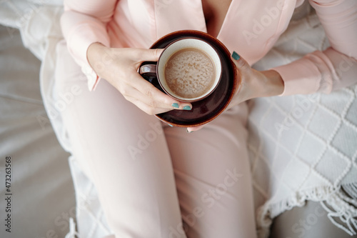 Woman in light pink pajamas holding cup of delicious cappunnino