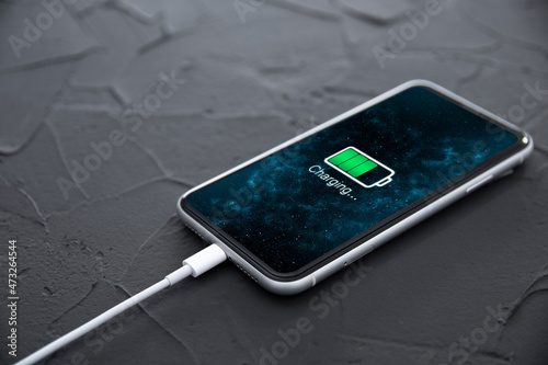 Mobile smart phone on wireless charging device on dark background. Icon battery and charging progress lighting on screen.smartphones connected to power source.low battery level problems.Plugged Phone