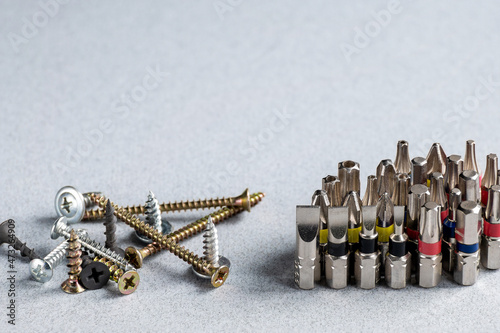 Screwdriver bits, electric screwdriver bits, different versions and various fasteners - screws, bolts, self-tapping screws on a grey background. Copy space.