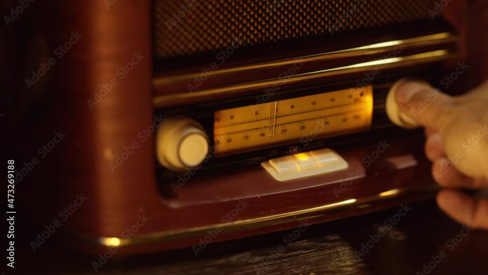 Vintage wooden retro radio receiver, macro shot of manual tuning of radio waves, hand turns the tuning knob. Slow camera movement from left to right.