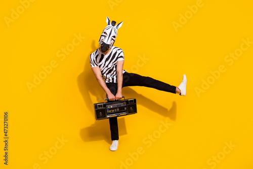 Photo of cheerful funny man wear zebra print t-shirt mask listening boombox dancing isolated yellow color background photo