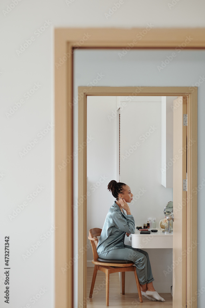 Beautiful woman in silk pajamas sitting in front of vanity and applying skincare and makeup Beautiful woman in silk pajamas sitting in front of vanity and applying skincare and makeup