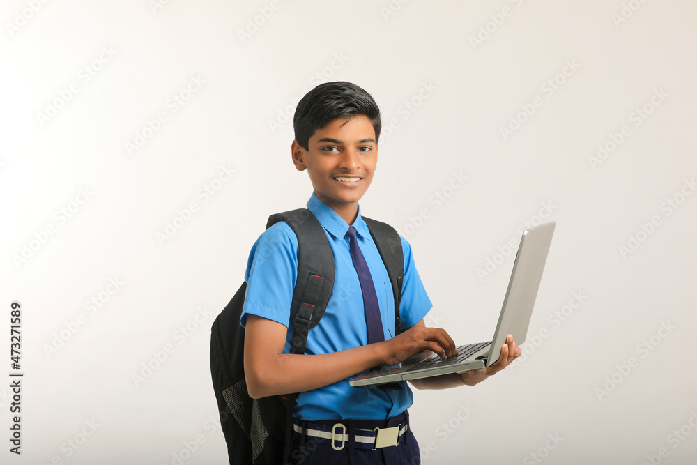 Indian school boy in uniform and using laptop on white background.