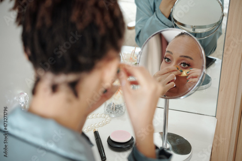 Beautiful woman applying anti-fatigue undereye patches in front of magnifying mirror photo