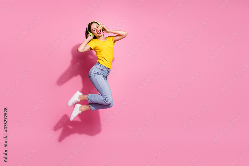 Photo of charming funny lady dressed yellow clothes enjoying songs arms earphones jumping high empty space isolated pink color background