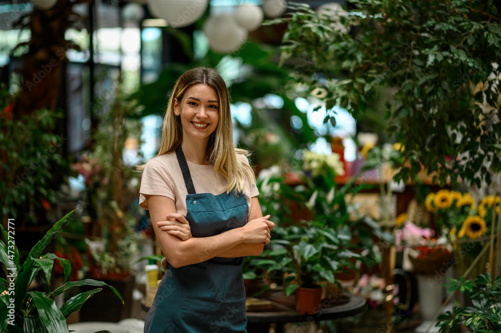 Florist working in flower shop while smiling and looking at a camera Florist working in flower shop while smiling and looking at a camera