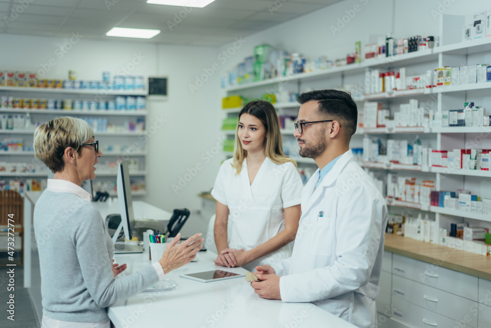 Two pharmacist giving prescription medications to senior female customer in a pharmacy Two pharmacist giving prescription medications to senior female customer in a pharmacy