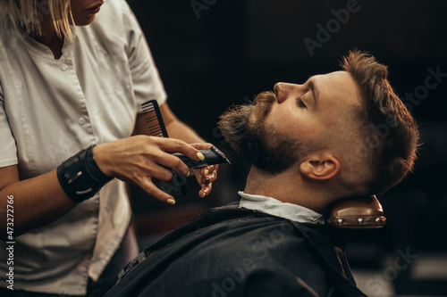 Young bearded man getting beard haircut by hairdresser