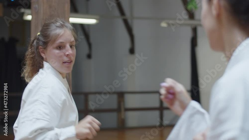 Handheld shot of focused girl fighting with her opponent in gym. Front view of excited martial artsist wearing kimono improving skills, demonstrating basic karate poses. Sport, sparring concept