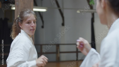 Handheld shot of focused girl fighting with her opponent in gym. Front view of excited martial artsist wearing kimono improving skills, demonstrating basic karate poses. Sport, sparring concept photo