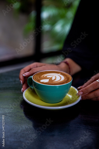 green mug of cappuccino with latte art on wooden background.