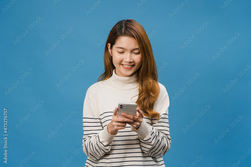 Young Asia lady using phone with positive expression, smiles broadly, dressed in casual clothing feeling happiness and standing isolated on blue background. Happy adorable glad woman rejoices success. Young Asia lady using phone with positive expression, smiles broadly, dressed in casual clothing feeling happiness and standing isolated on blue background. Happy adorable glad woman rejoices success.