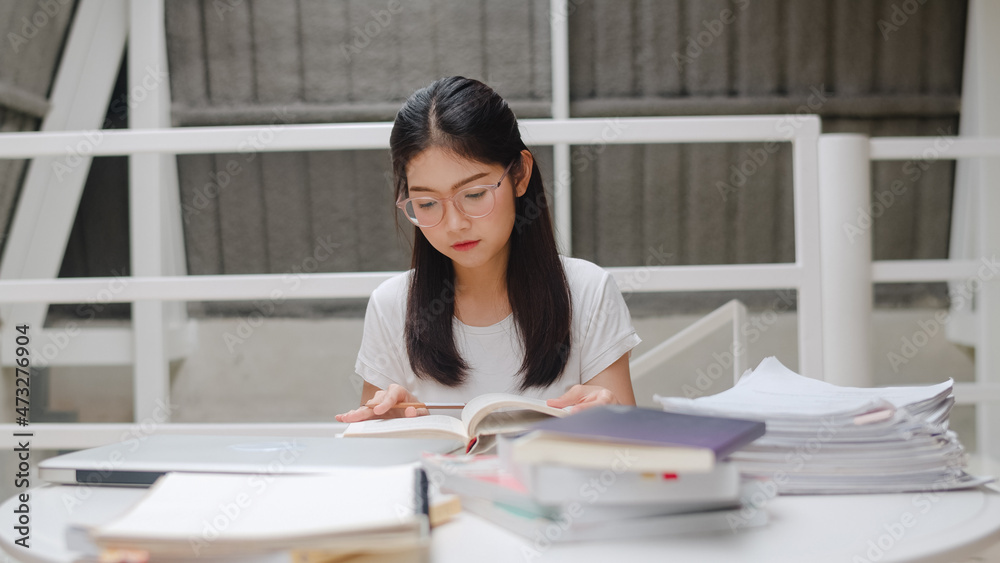 Asian student women reading books in library at university. Young undergraduate girl do homework, read textbook, study hard for knowledge and education on lecture desk at college campus. Asian student women reading books in library at university. Young undergraduate girl do homework, read textbook, study hard for knowledge and education on lecture desk at college campus.