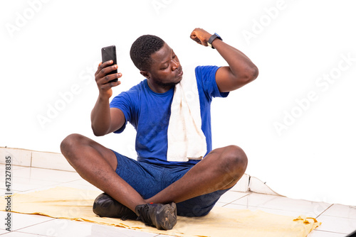young sporty man sitting down holding mobile phone and showing his biceps.