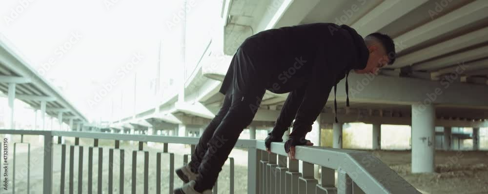 Arc shot of male athlete in sports outfit performing straddle planche on urban railing during street workout in city