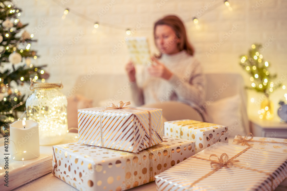 Woman sitting on couch near christmas tree and packing handmade gift boxes putting it on the table. Presents for family. Woman sitting on couch near christmas tree and packing handmade gift boxes putting it on the table. Presents for family.