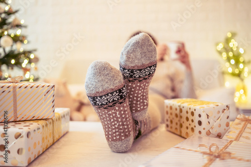 Unfocused, blur woman sitting and relaxation near christmas tree with cup of cocoa and marshmallows after finishing pakking gift boxes for family. photo