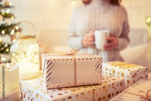 Unfocused, blur woman sitting and relaxation near christmas tree with cup of cocoa and marshmallows after finishing pakking gift boxes for family. photo