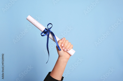 Student holding rolled diploma with ribbon on light blue background, closeup photo
