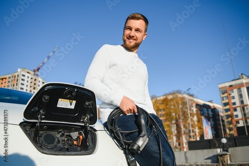 Stylish man inserts plug into the electric car charging socket photo